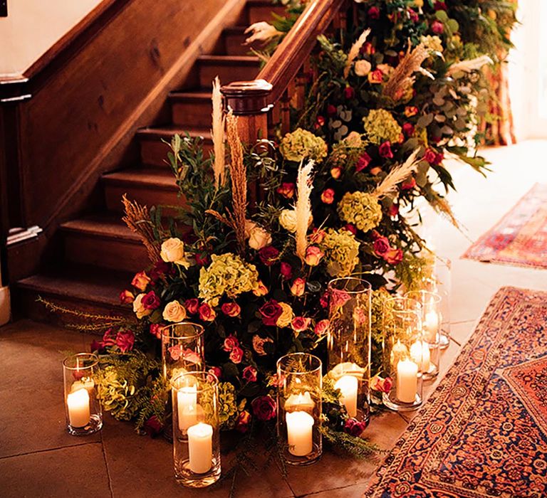 Red roses, hydrangeas and papas grass decorating the staircase with white pillar candles in hurricane vases at Iscoyd Park 