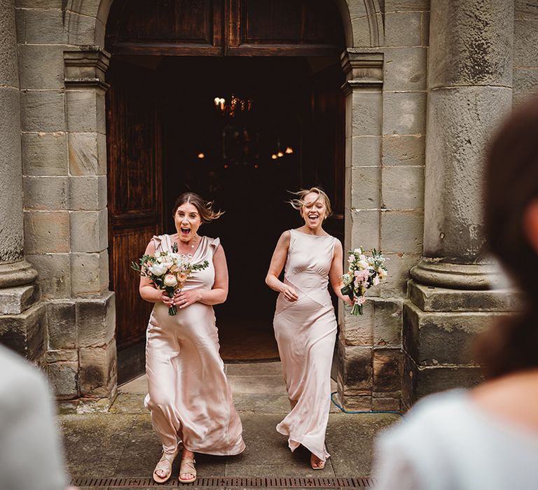 Bridesmaids in light pink satin look mismatched bridesmaid dresses coming out of the church