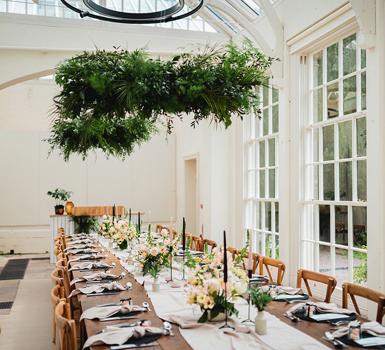 Neutral and botanical wedding tablescape with festoon chandelier, large suspended foliage decor, tapered candles and lots of greenery