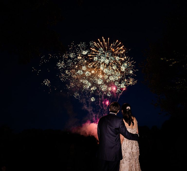 Bride & groom watch colourful reception fireworks outdoors 