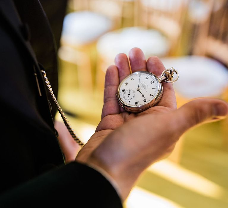 Groom takes a look at his silver pocket watch for one of his groom's accessories 