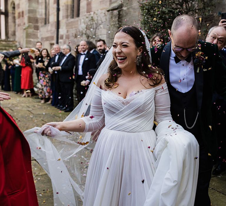 Bride in an elegant Watters wedding dress laughing with the groom during their confetti exit from their civil ceremony at Brinsop Court Manor House and Barn