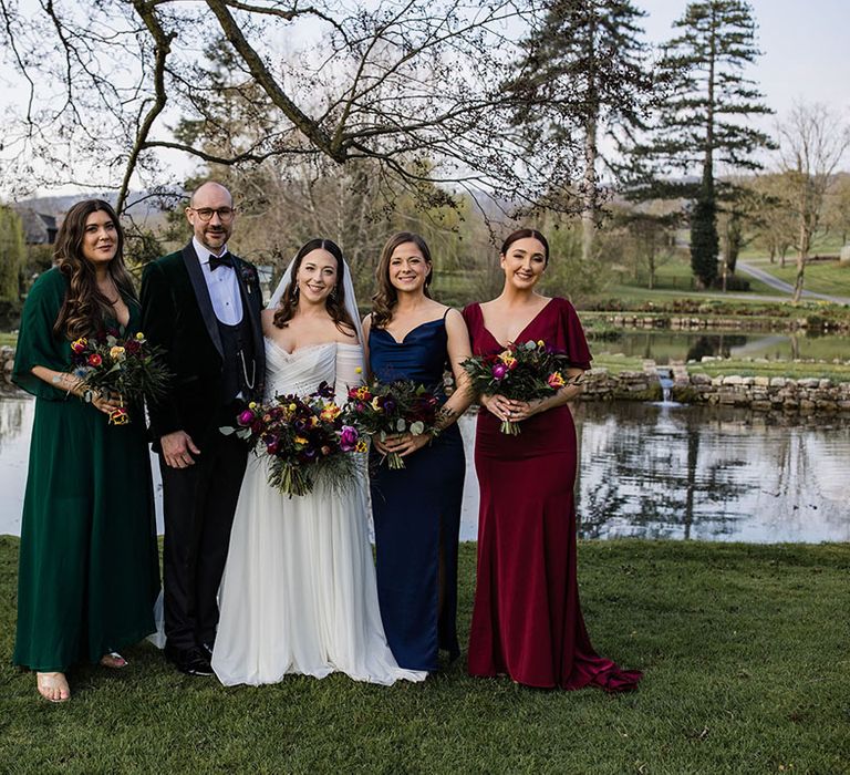 Bridesmaids in mismatched bridesmaid dresses in different colours and jewel tones for the spring wedding smiling with the bride and groom 