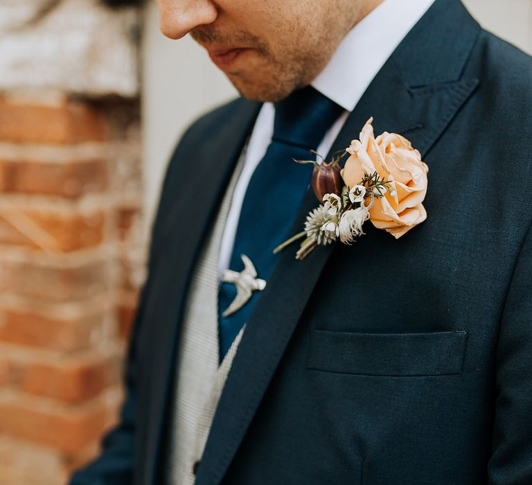 Groom in navy suit with blue tie with silver bird tie clip and pink rose buttonhole for rustic luxe wedding 