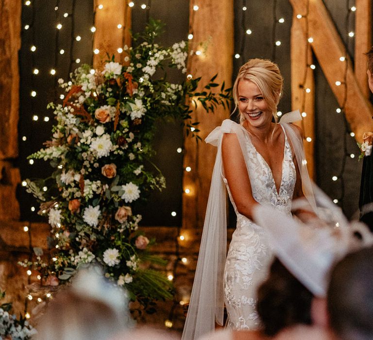 Smiling bride in Made With Love wedding dress with tulle wings and bow straps stands holding hands with the groom at the altar for the ceremony