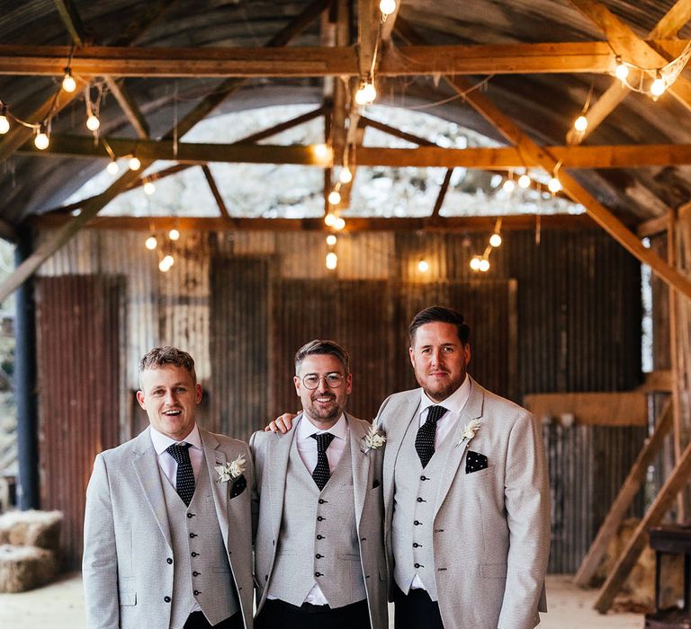 The groom and groomsmen standing together in light grey suit jacket and waistcoat with polka dot ties and handkerchief with white rose buttonhole