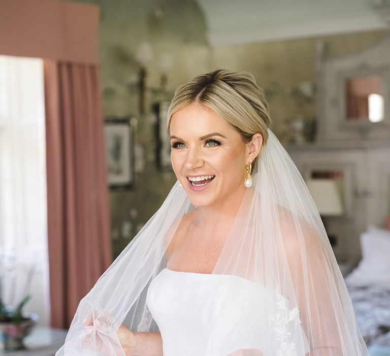 Bride with blonde hair in an updo wearing an embroidered edge wedding veil with pearl earrings 