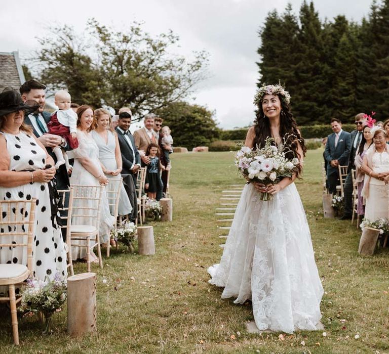 Bride wearing ethereal, celestial 3d appliqué sheer overlay wedding dress and bridal flower crown holding large white rose, peony, dried flower and foliage bridal bouquet walking down the aisle 