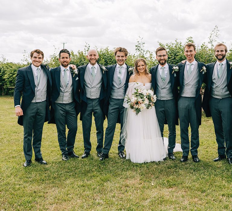 All the groom and groomsmen in matching outfits with green ties standing with the bride 