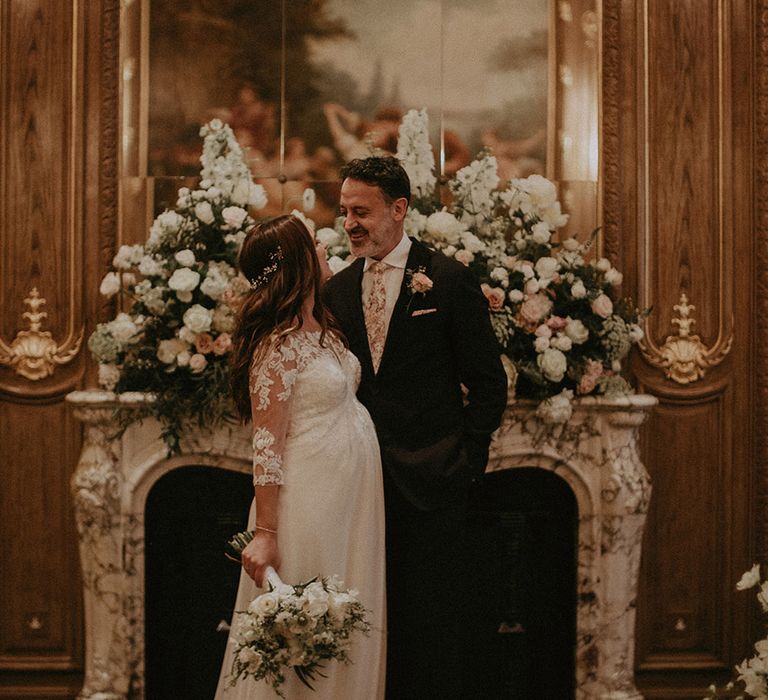 7 month pregnant bride in lace wedding dress with white bouquet with the groom in navy suit and floral tie at Claridge's wedding 