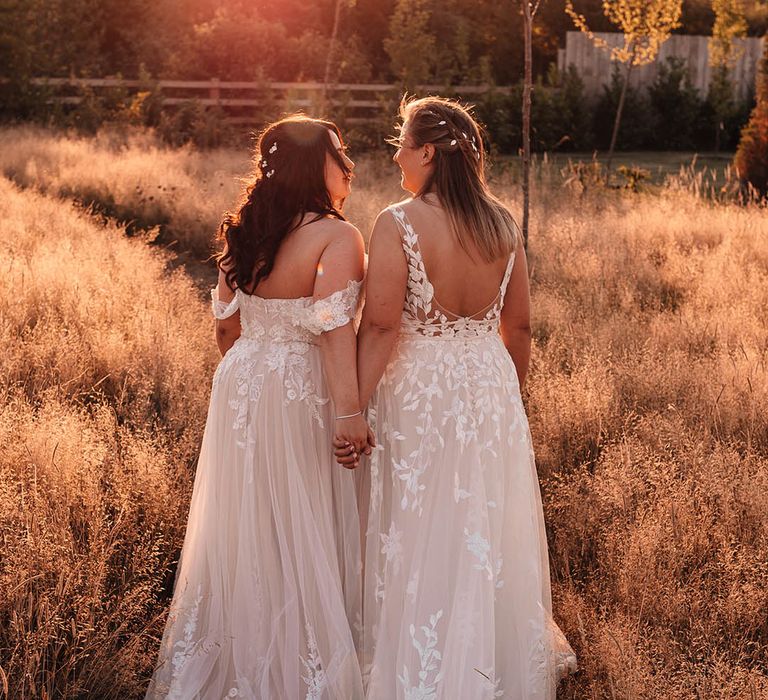 Two brides holding hands both wearing lace bridal gowns with silver hair accessories in for the barn wedding 