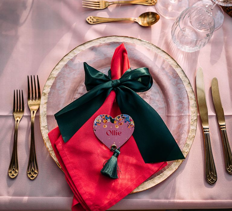 Marble wedding plates with bright pink napkins and dark green ribbon with heart place names, gold cutlery and coloured glassware 