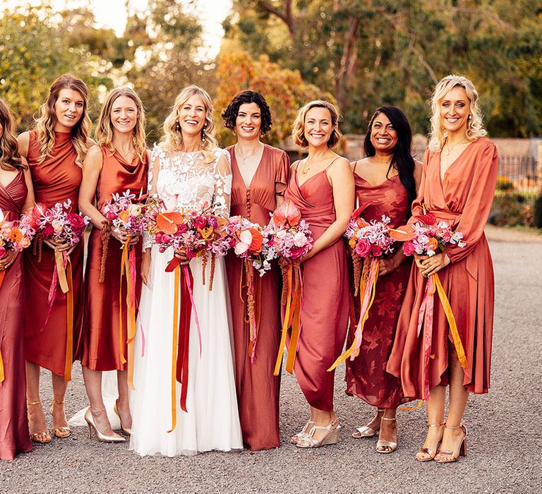 Mismatched orange bridesmaid dresses in a variety of styles with bride in lace long sleeve wedding dress 