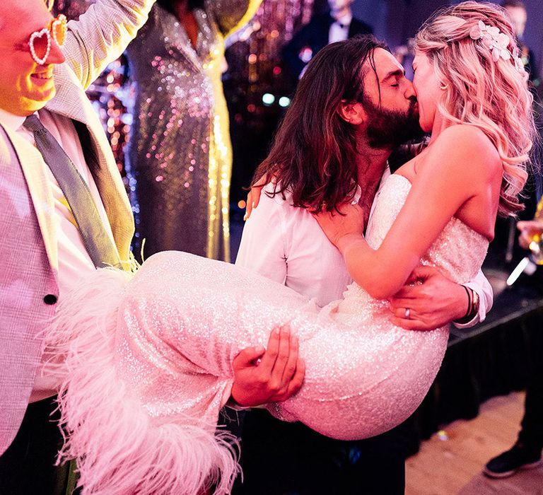 Bride in sequinned wedding dress with feathers kissing groom in white shirt