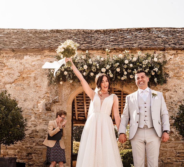 bride in a sparkly wedding dress and groom in a grey check suit at Caswell House outdoor ceremony with kick the bucket Bulgarian wedding traditions 