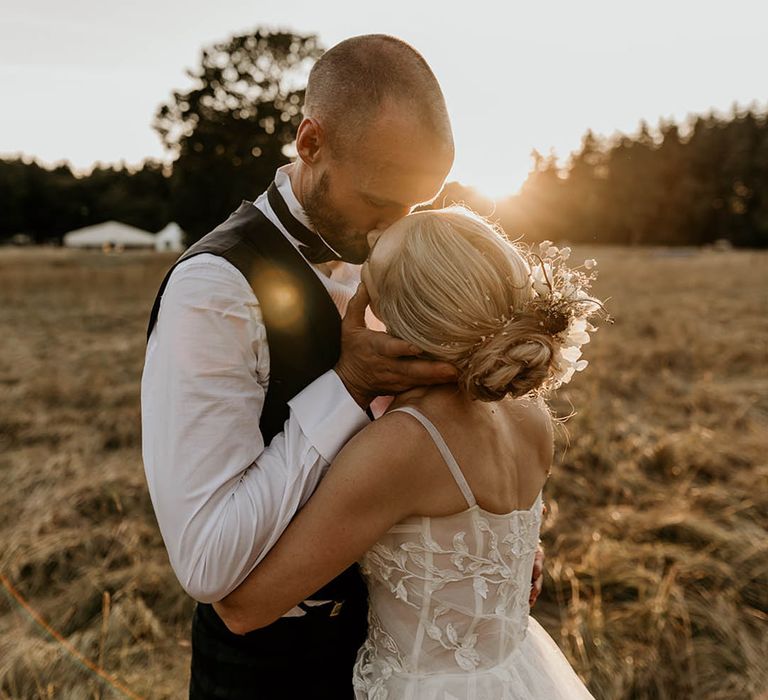 Golden hour wedding photo of the bride and groom at sunset with the bride wearing white flower hair accessory 