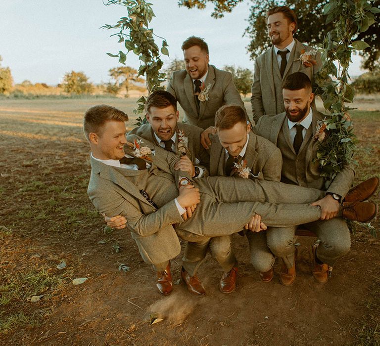 The groom lays across the groomsmen on a wooden swing at the Wales wedding venue 