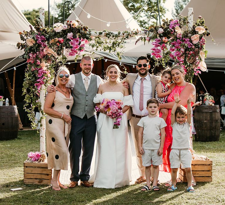 Pink wedding flower arch decorating the entrance to the tipi with the wedding guests