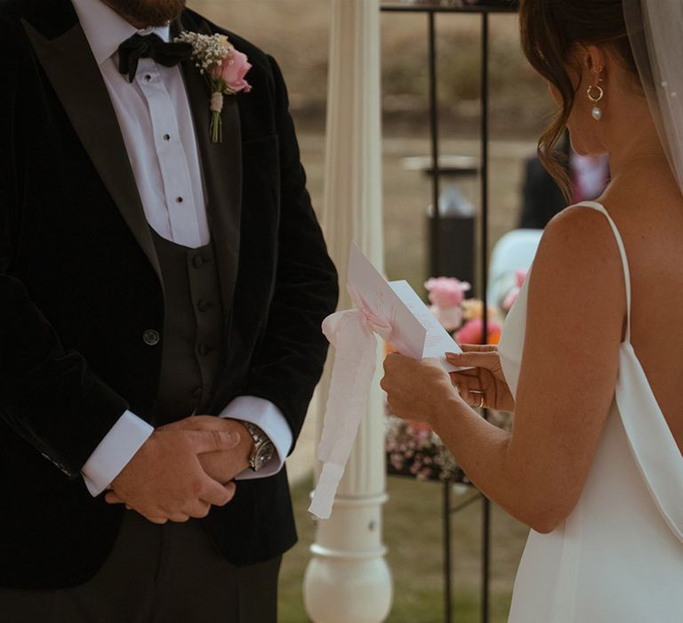 Bride in satin wedding dress with open back style and pearl wedding veil exchanging vows with the groom 