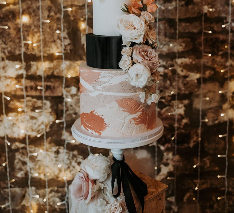 Black, white, and pink wedding cake decoration in front of fairy lights 