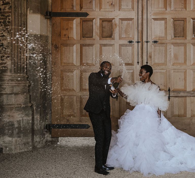 Bride in tulle wedding dress with long train posing with the groom in a black tuxedo for wedding photo 