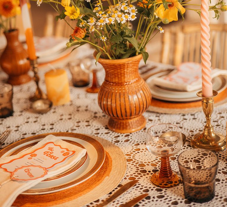 Terracotta vase with orange and yellow wedding flowers with textured and patterned candles and taper candles 