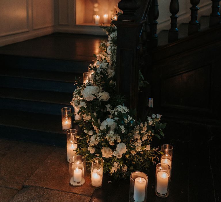 Hurricane vases of candles with white wedding flowers decorating the staircase 