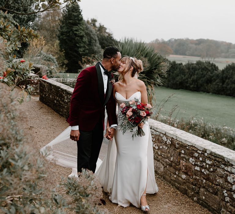 Groom in red velvet tuxedo kissing the bride in a strapless wedding dress by Jane Hill 