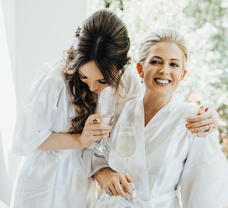 Two brides in white robes getting ready for their wedding day together in Santorini 