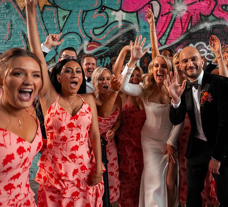 Wedding party wearing pink and red patterned bridesmaid dresses with the groomsmen in black tuxedos at city wedding 