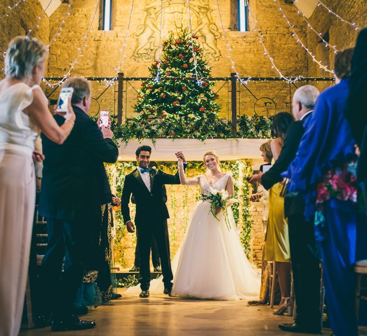 Bride and groom standing at the altar just married with Christmas tree and fairy lights decor 