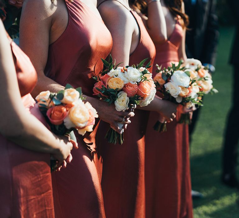 Bridesmaids holding peach and ivory rose bouquets 