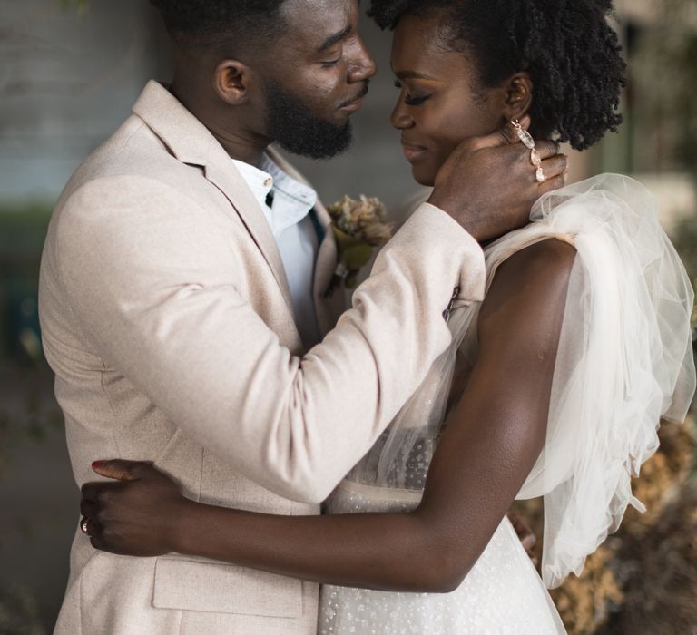 Portrait of the groom in a beige wedding suit embracing his brides face 