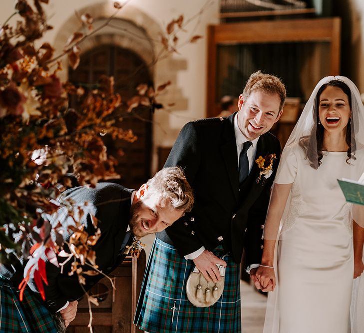 Bride and groom laugh with groomsman and Vicar during wedding ceremony