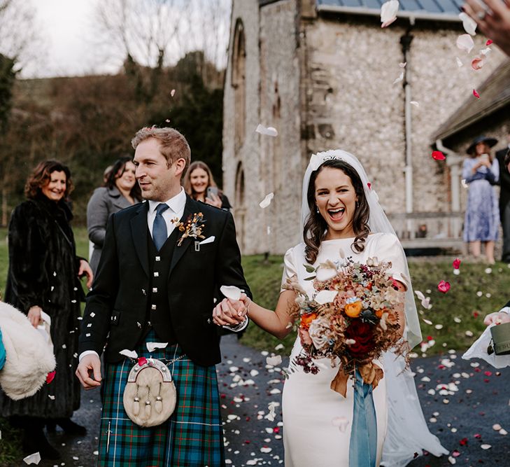 Bride and groom leave Christmas church wedding flowers ceremony hand in hand laughing.