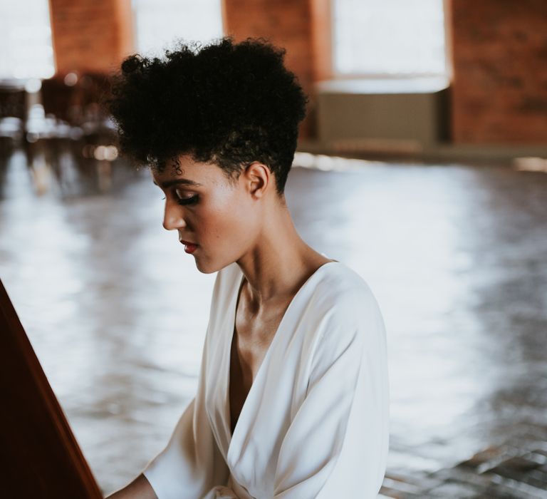 A bride with curly hair sits at a piano.