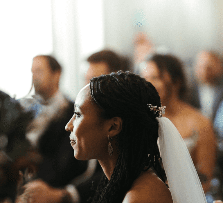 A Black bride sits in her wedding ceremony with loose braids in half up half down style