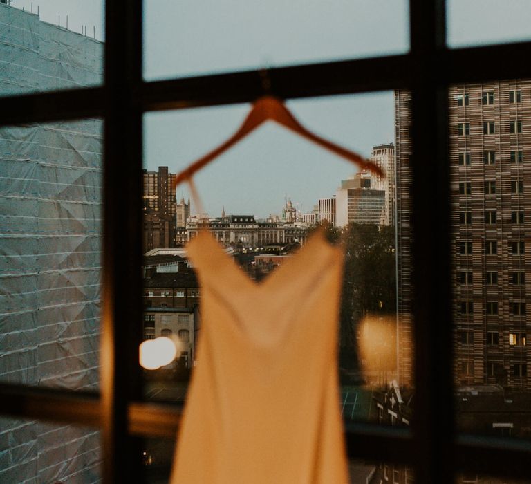 Simple silk wedding dress hanging from window pane