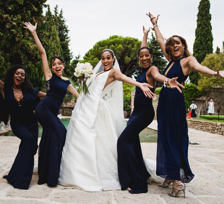 The bride and her bride squad, all wearing long navy blue bridesmaids dresses