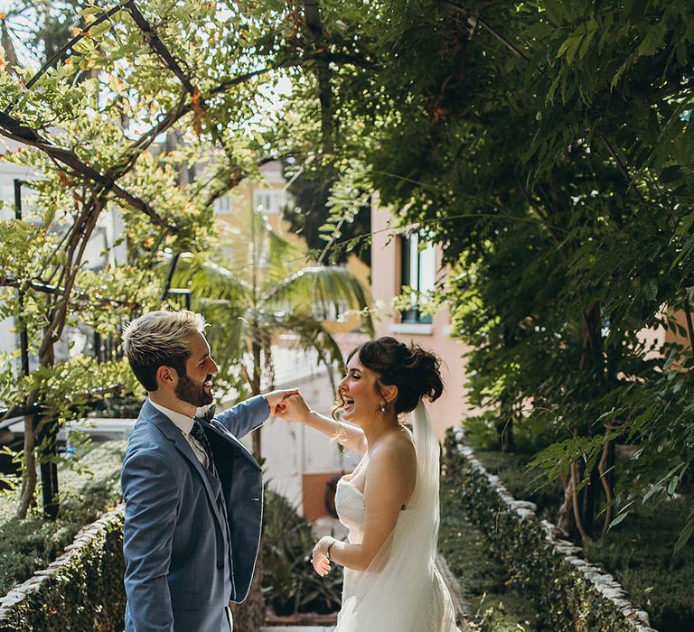 Groom in a three-piece light blue suit twirling his bride in a strapless wedding dress 