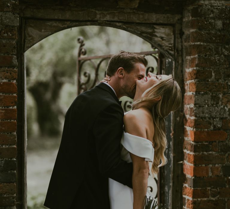 Groom kisses brides neck as she holds coral bouquet