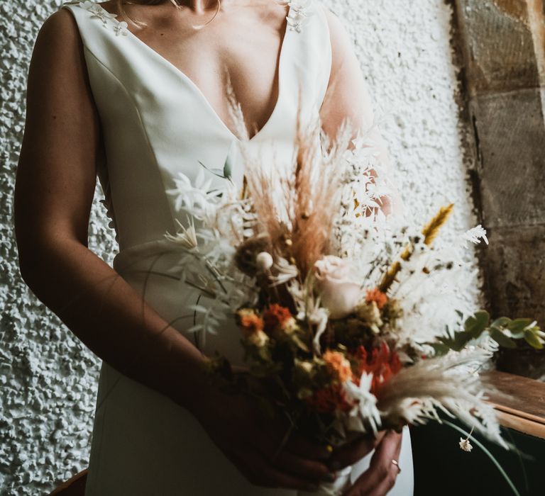 Bride stands in the window whilst holding floral bouquet on the morning of her wedding