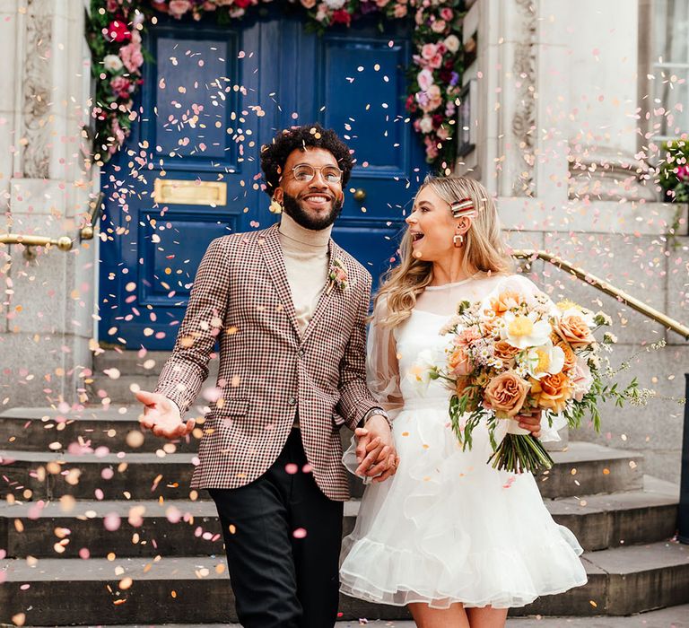 Stylish bride and groom confetti moment at Chelsea micro wedding with blue door decorated in flowers 