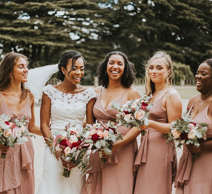 Bridal party portrait with bridesmaids in blush pink dresses and bride in a lace wedding dress holding red and white bouquets