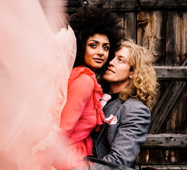 Groom in a grey suit looking at his bride in a red dress 