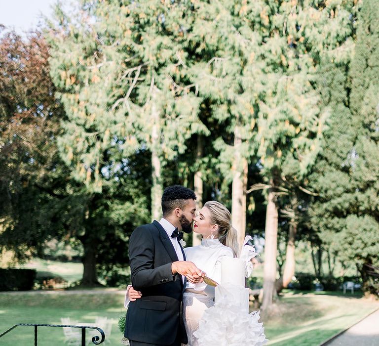 Bride and groom cutting the all white wedding cake outside 