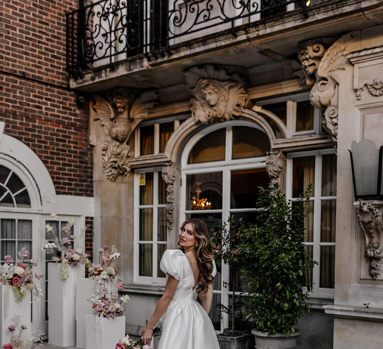 Bride in a taffeta Love In Lave bridal gown with puff sleeves standing in the courtyard at Dartmouth House wedding venue in Mayfair