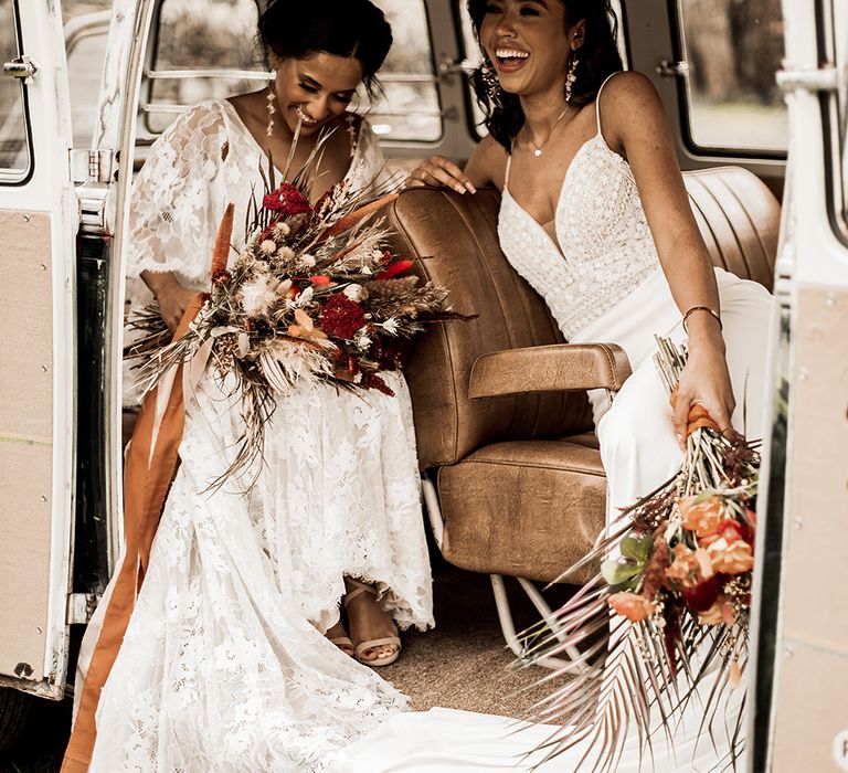 Two brides sitting in a VW camper van holding red dried and fresh flower bouquets 