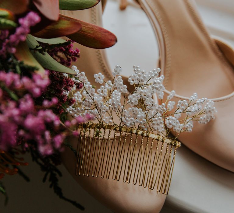 Pearl comb resting on nude strapped heels next to pink flowers before barn wedding ceremony 