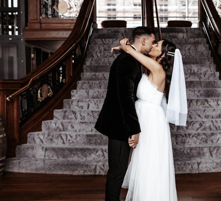 Bride & groom kiss at the end of staircase on the morning of their wedding day after first look moment